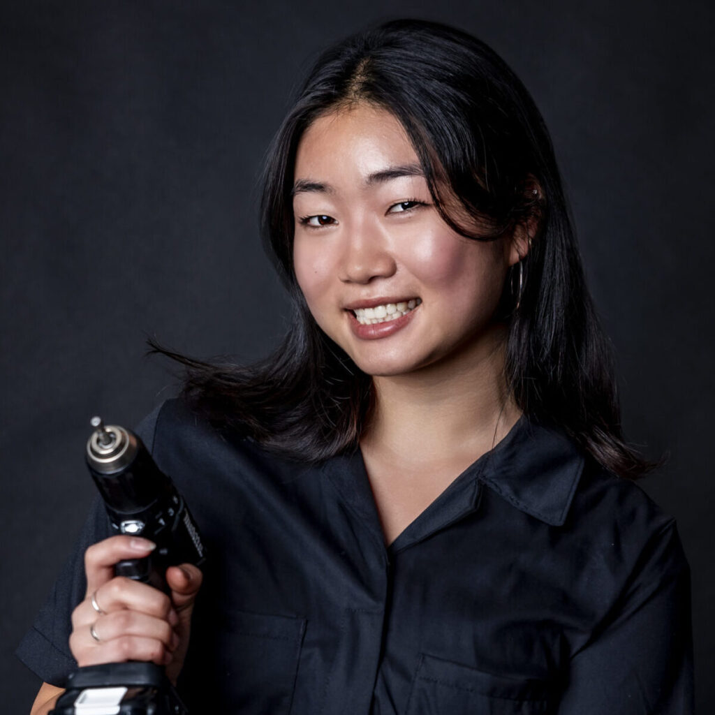 woman in black jumpsuit holding a drill smiling