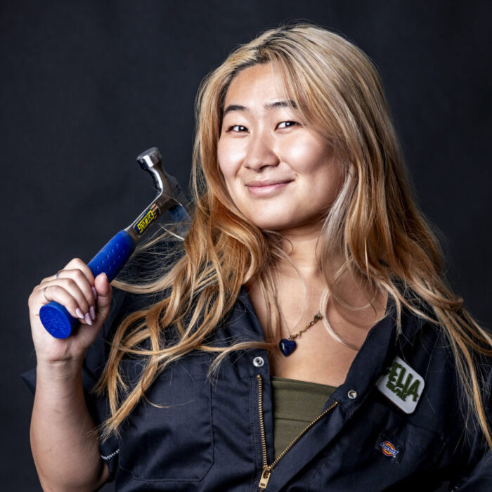 woman in black jumpsuit smiling holding a hammer