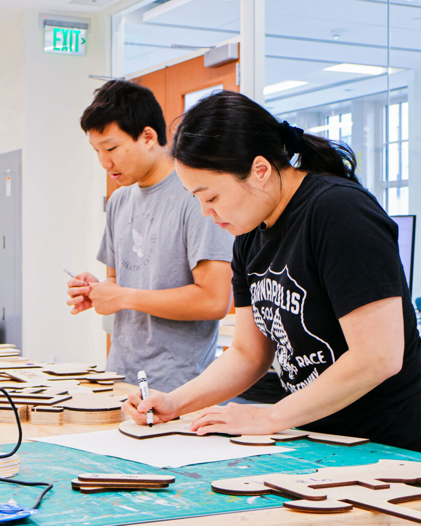 Professor and student working in prototyping studio, using markers to sketch on cut-out pieces of wood.