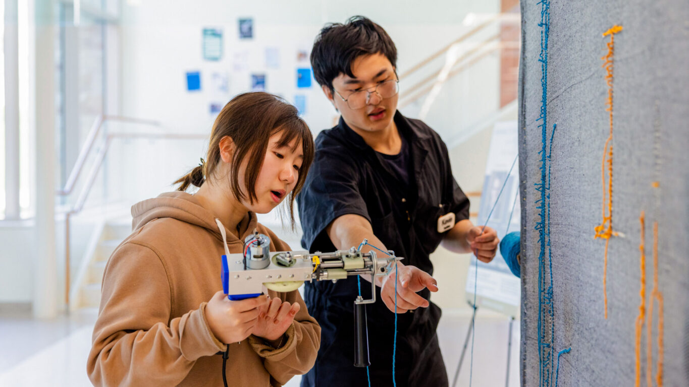 Student worker and a BC student in a training session using a tufting machine, creating a rug